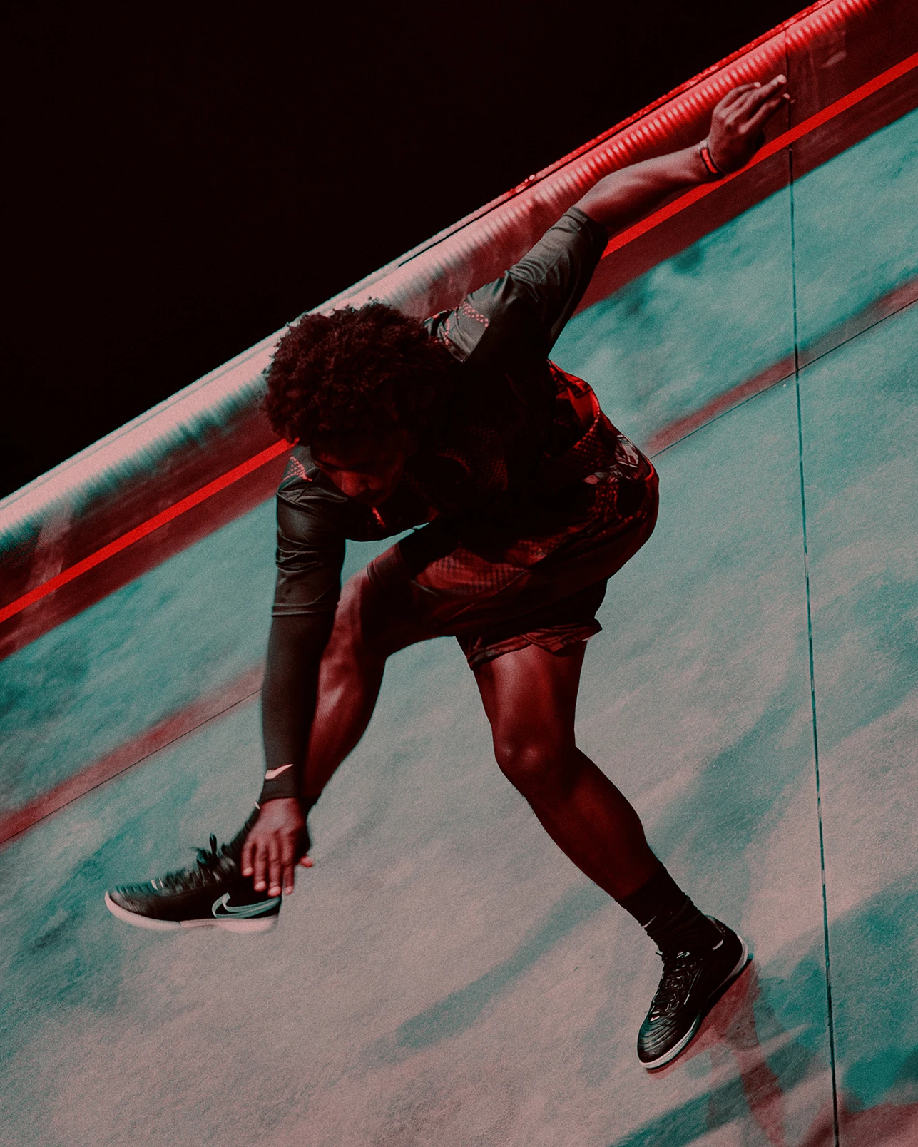 A person wearing athletic clothes and sneakers performs an acrobatic move on a sloped, smooth surface under dramatic lighting.