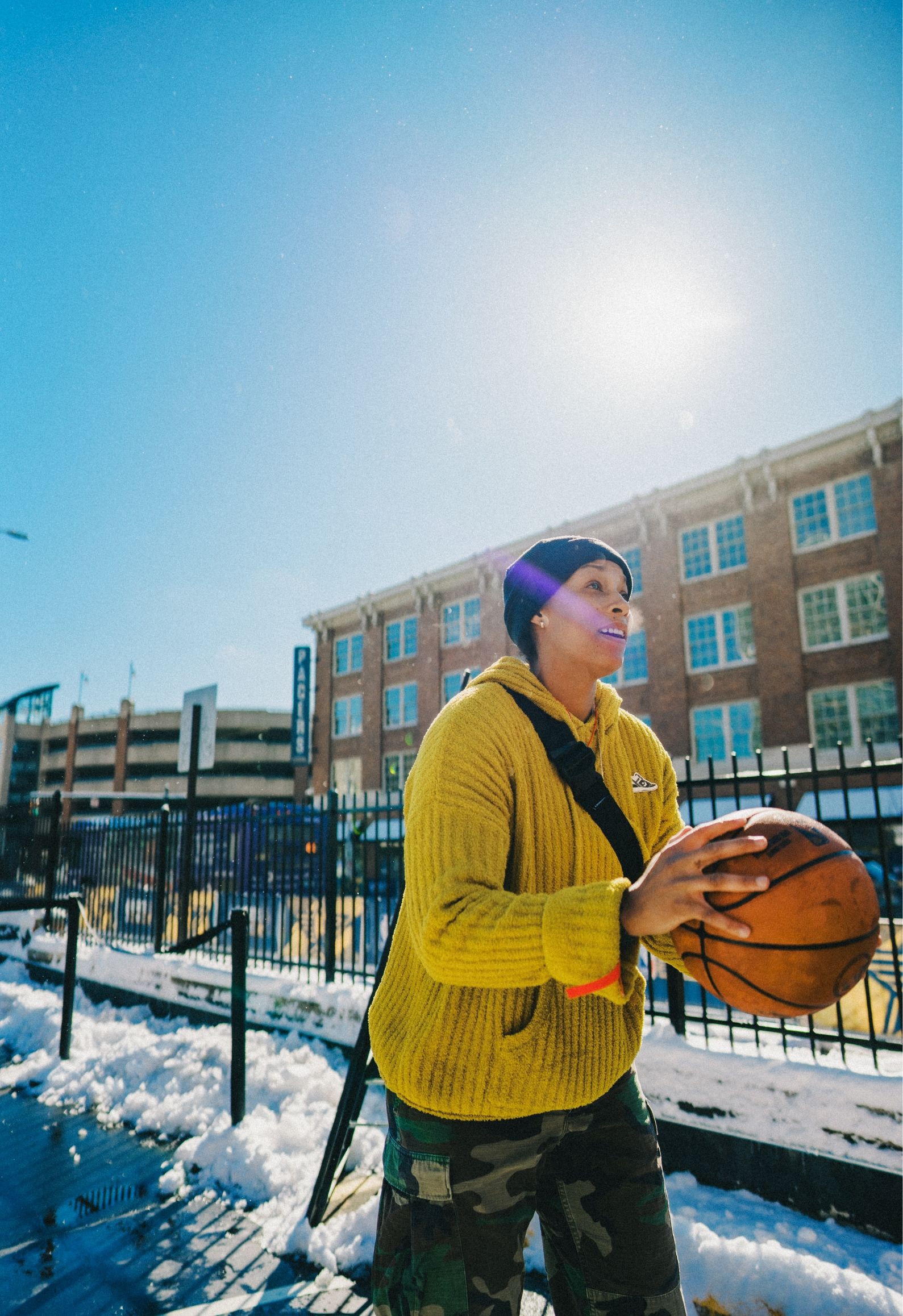 person gets ready to shoot basketball with a blue sunny sky background and snow on the ground