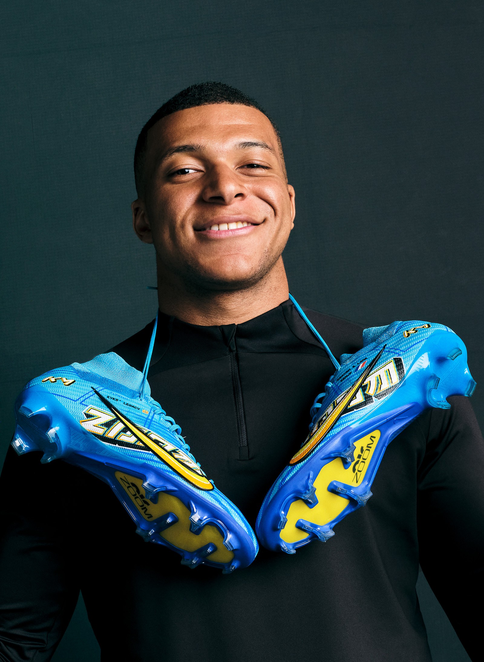 Mbappe smiling with new Nike Air zoom boots around his neck