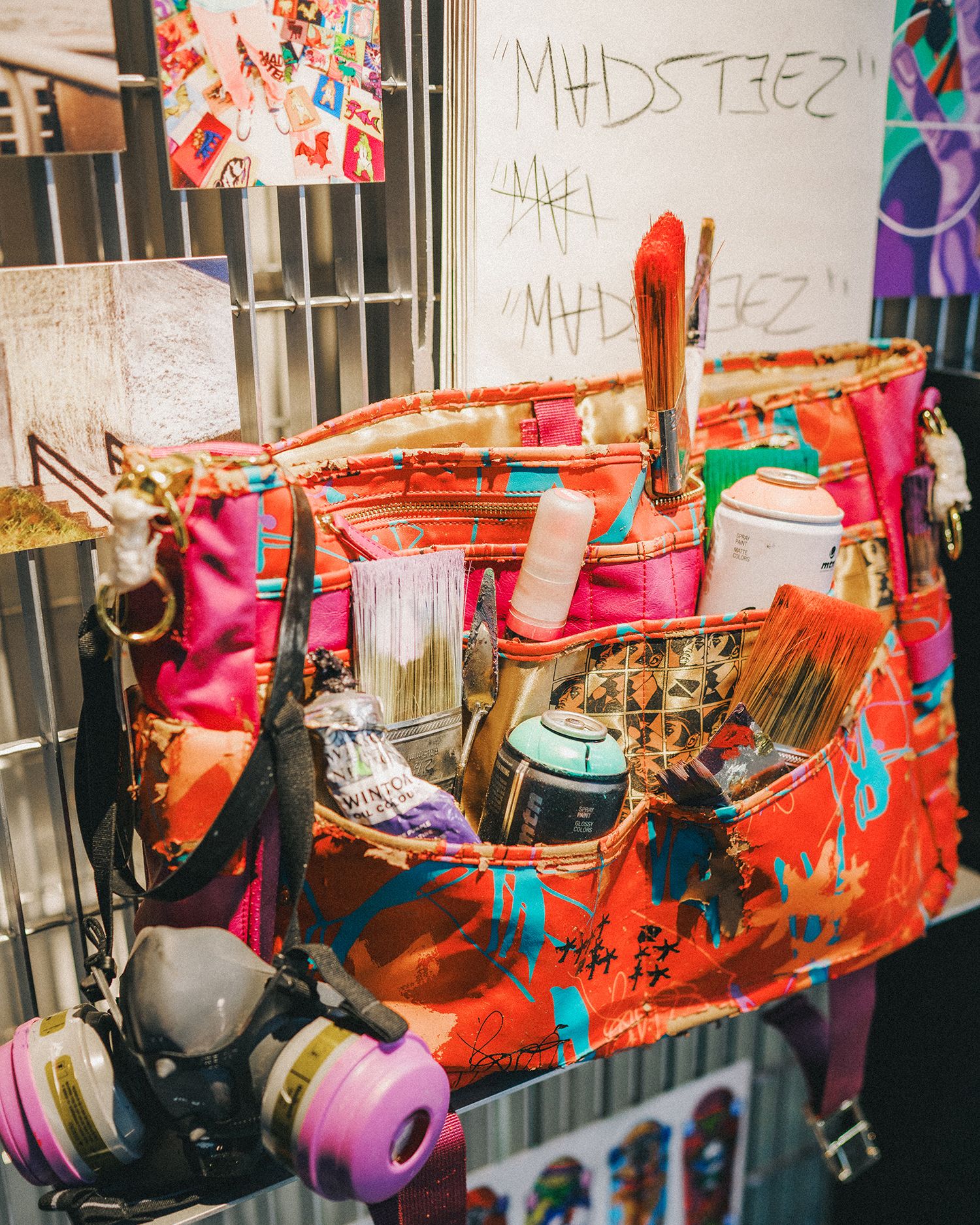 close up of Madsteez's tool pouch with spraycans, masks, and other paint supplies all with colorful paint splattered on them