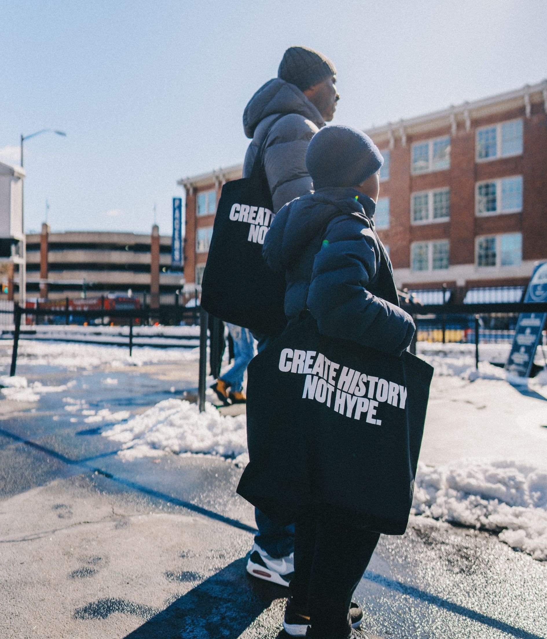 Man and boy look off towards the right. Both have totle bag that says Create History Not Hype