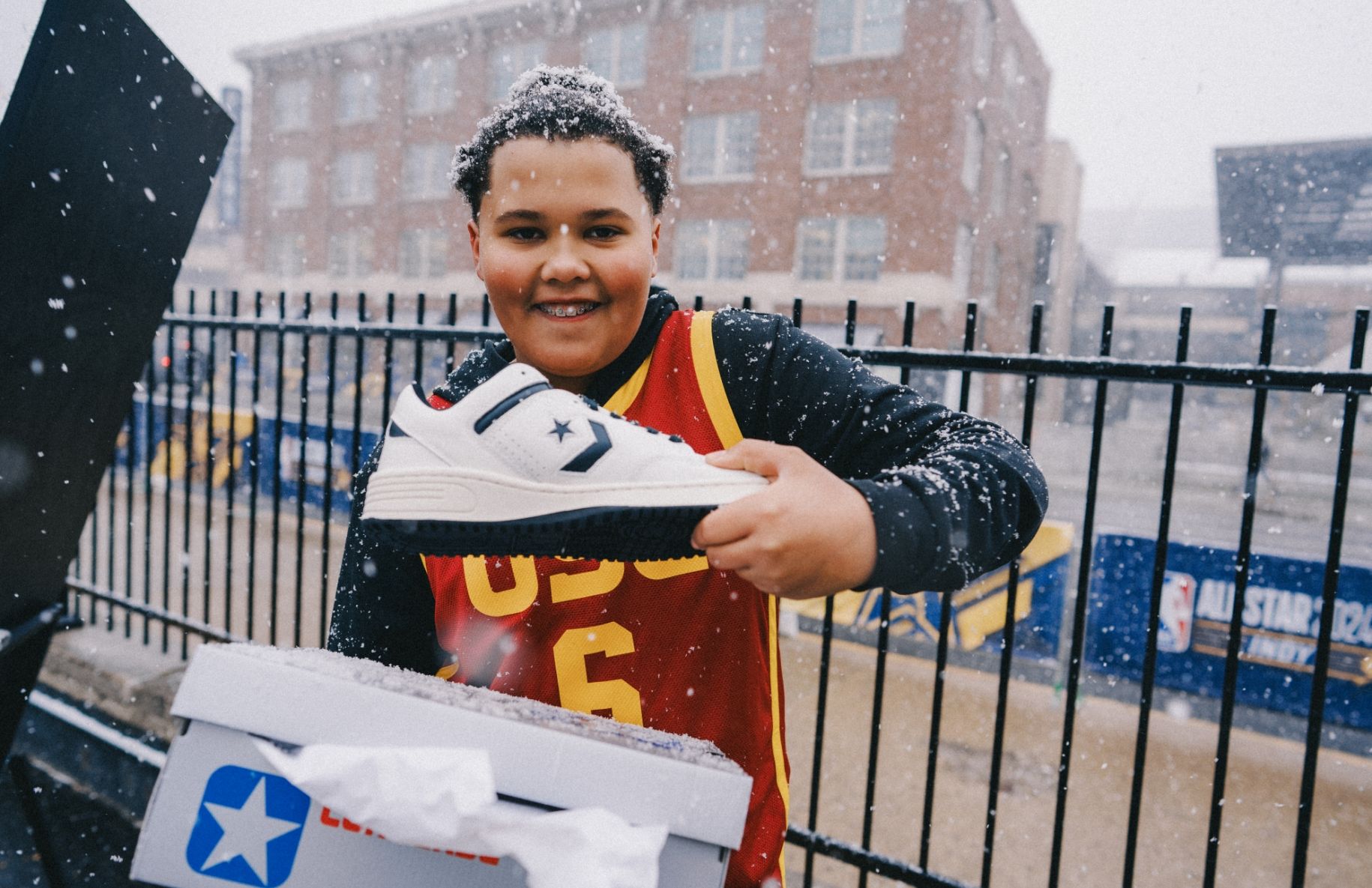 Young person smiles and holds up a converse sneaker out of the box. it is snowing.