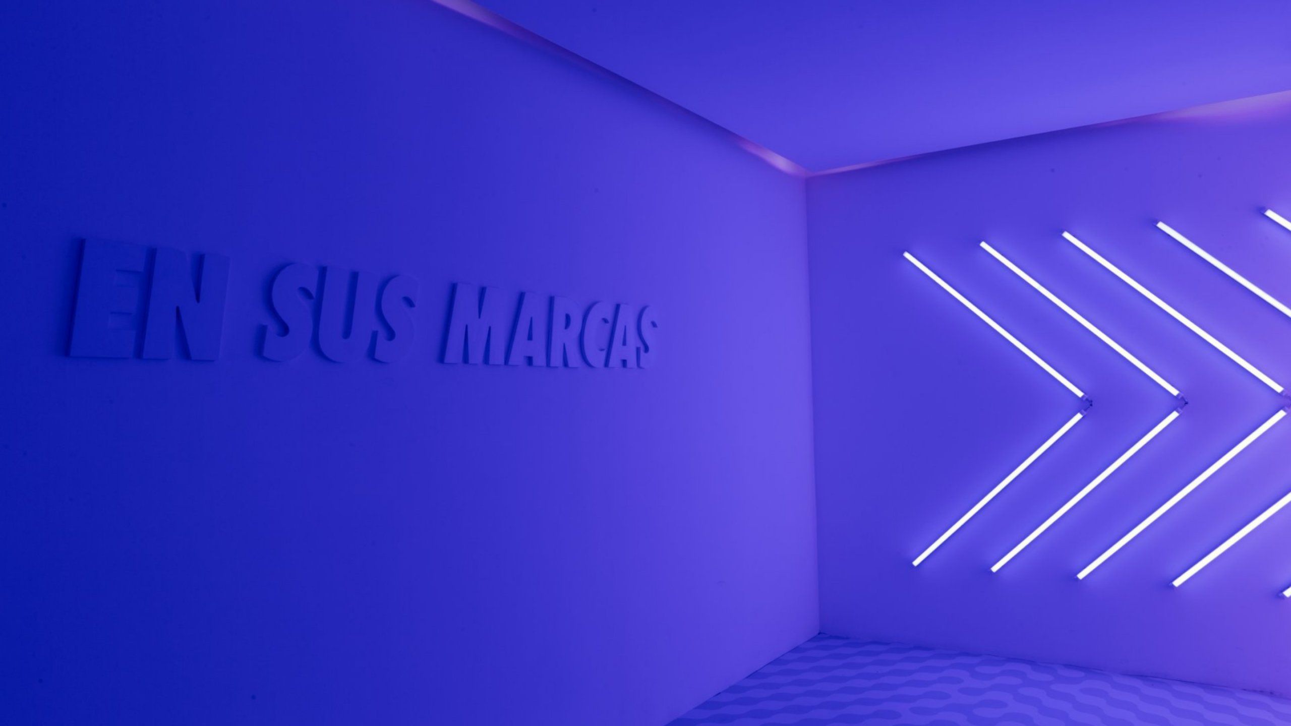 Purple room in installation. Zig zag carpet like sole of Nike React shoe, one wall has neon arrows, the other wall has text En sus marcas