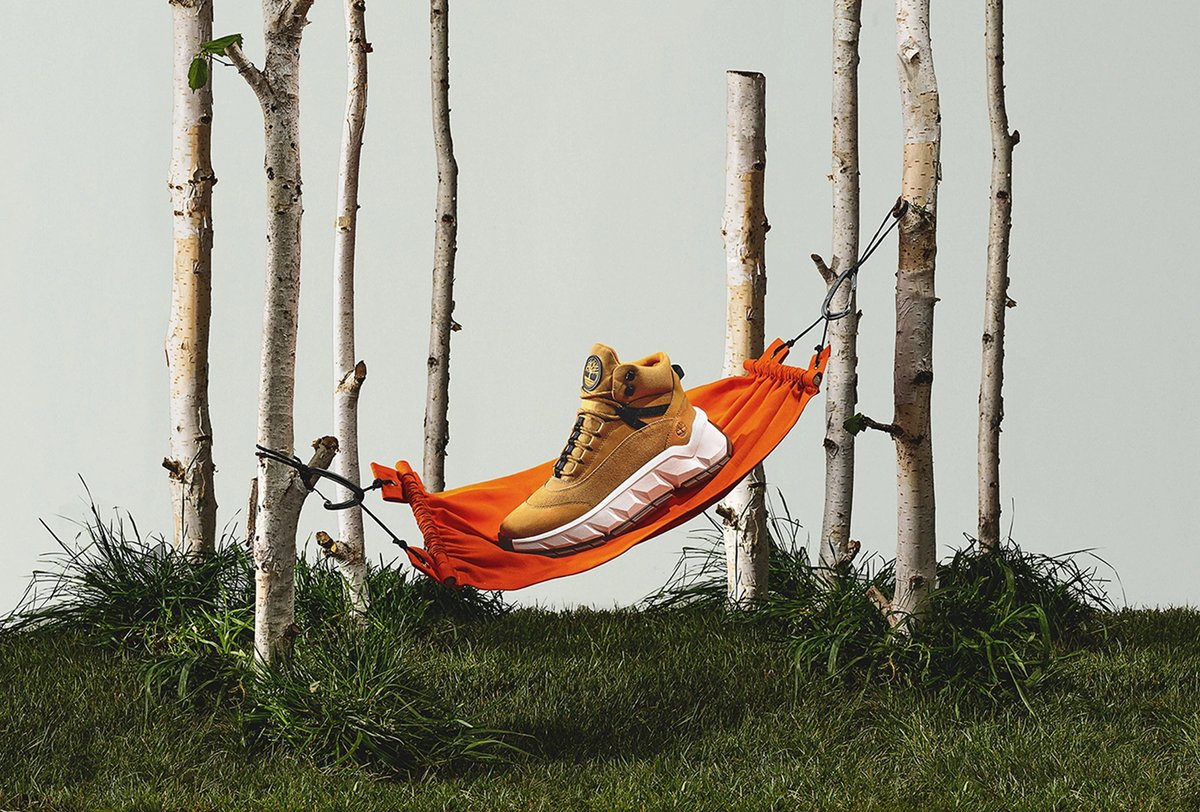 A tan and white high-top sneaker rests on an orange hammock suspended between birch trees over green grass.