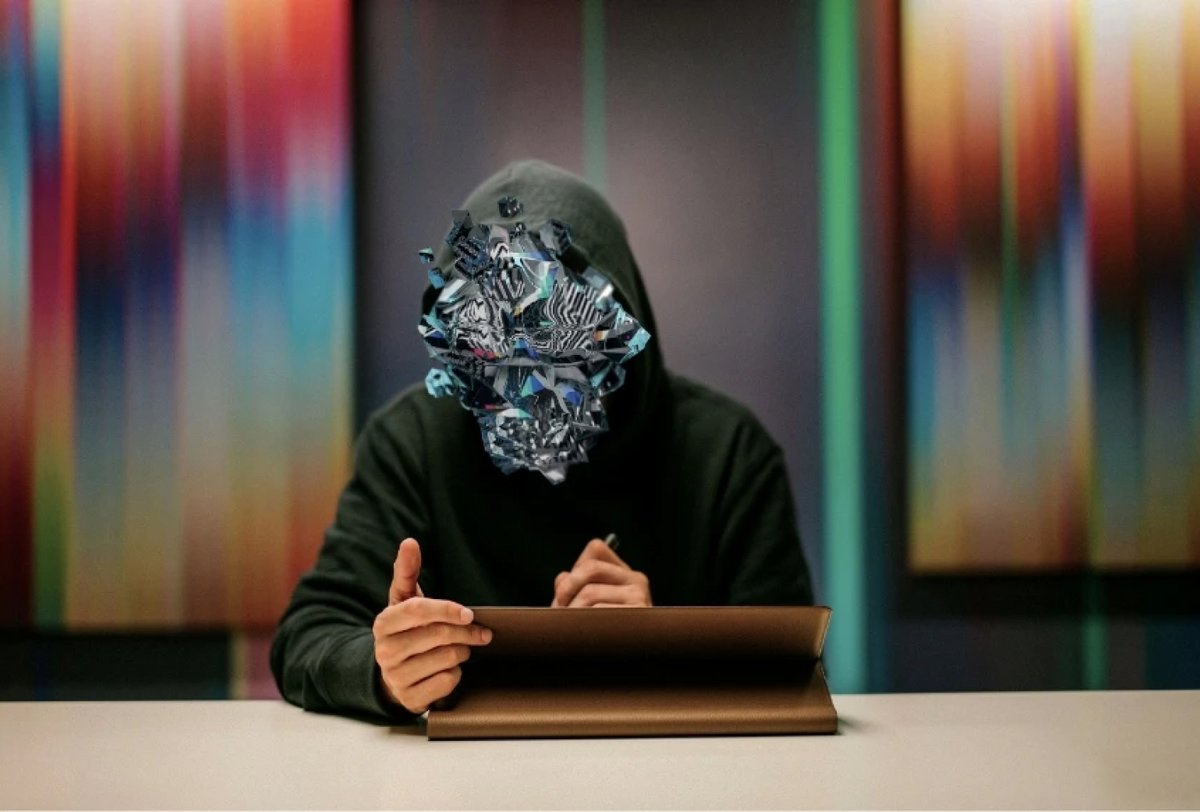 A person in a hooded sweatshirt sits at a desk using a tablet, with their face replaced by a digital, abstract geometric design.