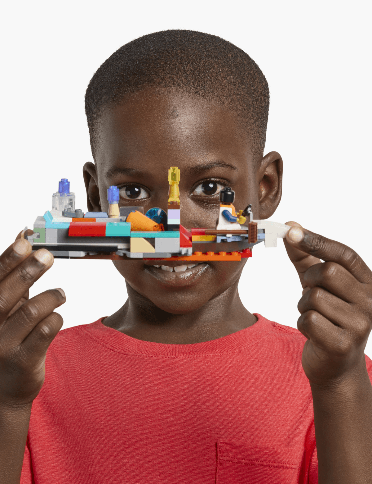 A child in a red shirt holds a colorful LEGO creation up to their face, smiling.