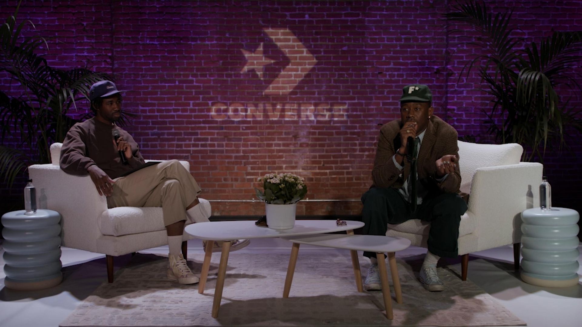 Tyler the Creator and John Boyega sitting having talk with microphone and converse logo on brick wall behind them