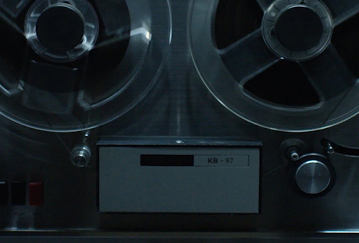 Close-up of a vintage reel-to-reel tape recorder with two large reels, control knobs, and a label marked "KB-97" on the front panel.