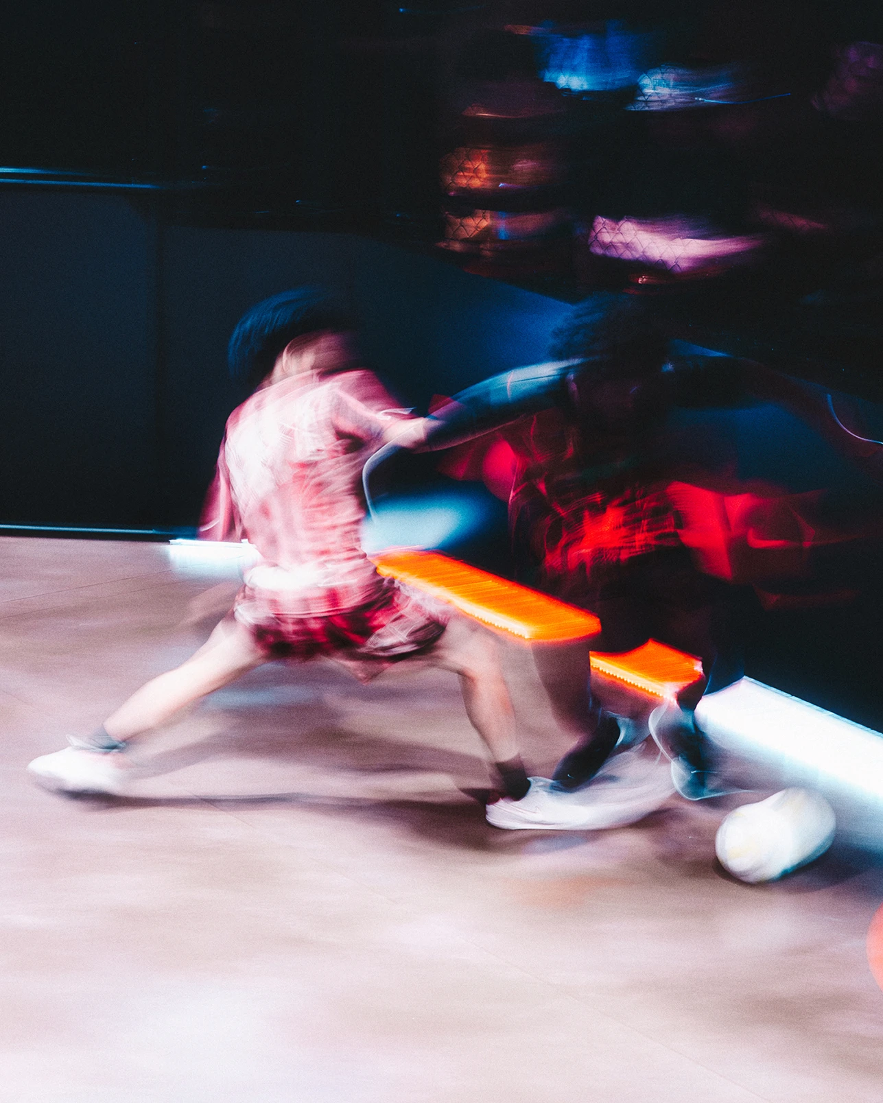 Two people playing indoor soccer, both in motion blur, with a white soccer ball near their feet on a polished floor.