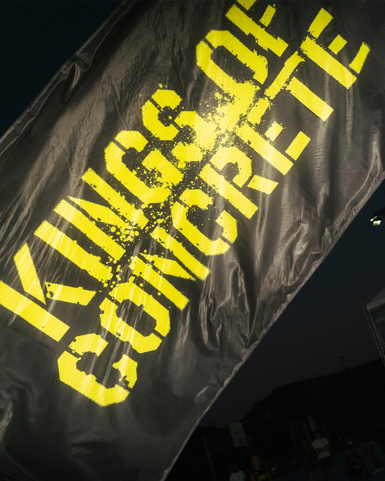 A black flag with bold yellow text reading “KINGS OF CONCRETE” against a dark background.