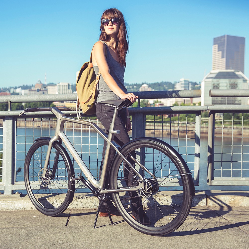 woman stands at city water front with bicycle