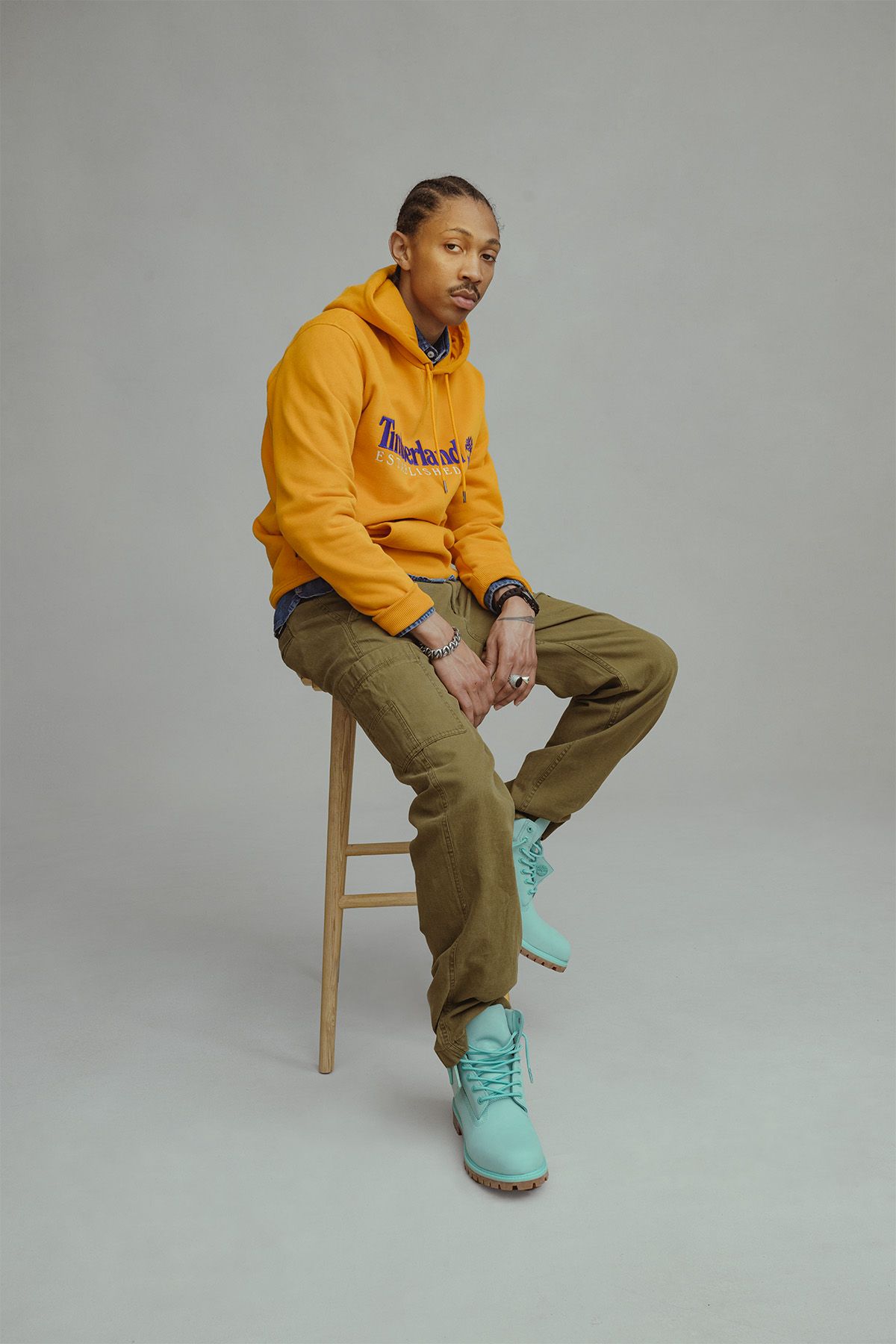 Man sitting in chare with orange Timberland sweatshirt and Holiday light blue colorway Timberland boots