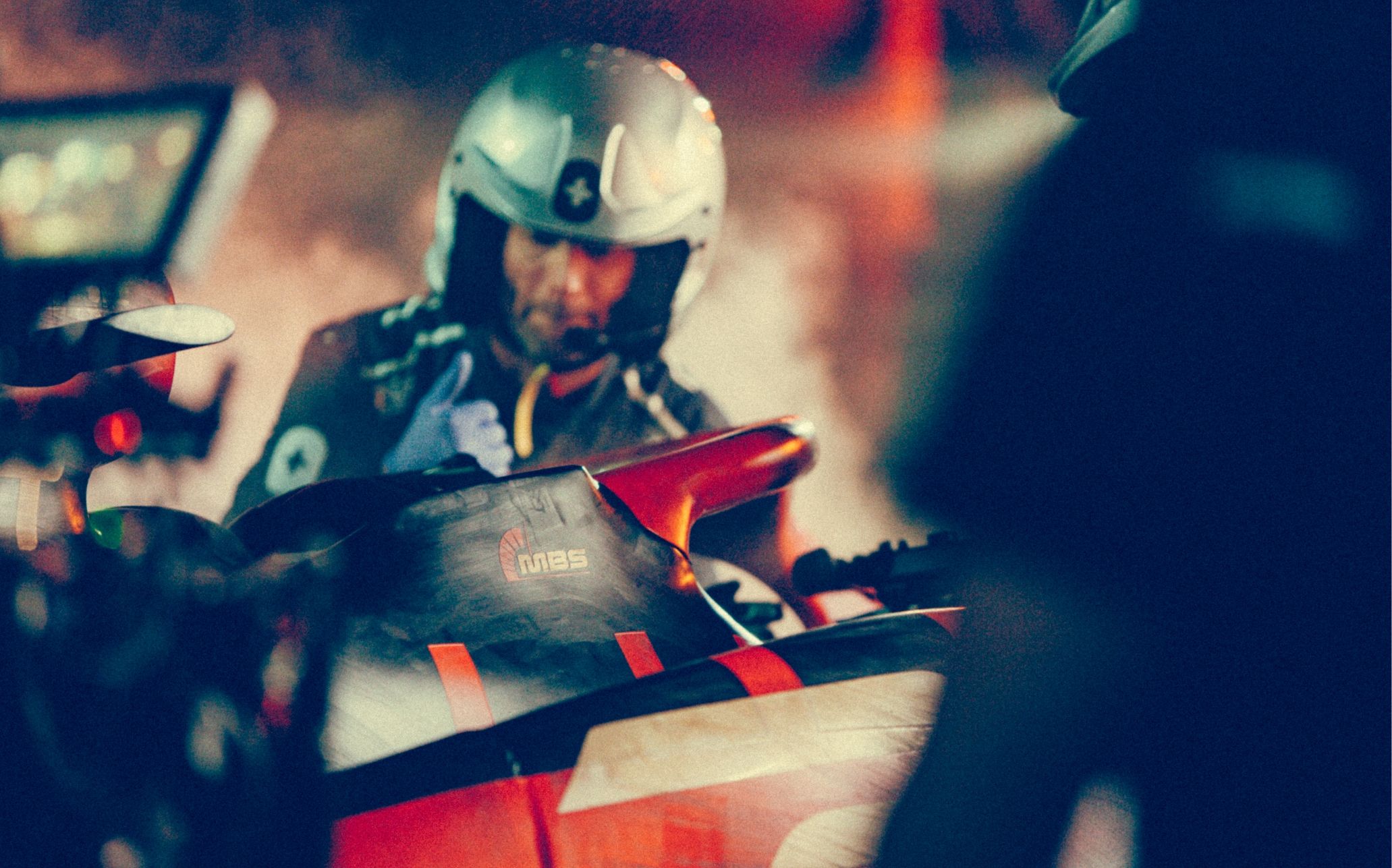 A person in a helmet interacts with a racing vehicle in a dimly lit setting.