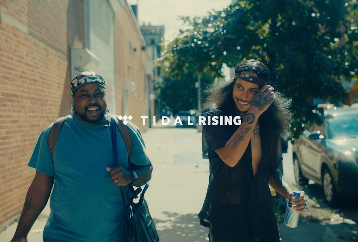 Two men walk outdoors on a sunny day, smiling and carrying bags, with “Tidal Rising” text displayed in the center of the image.