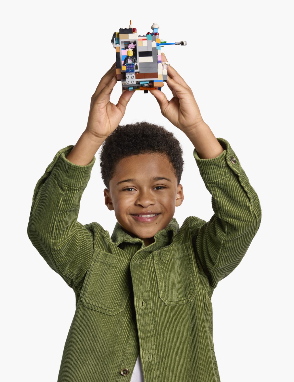 A child wearing a green shirt holds a LEGO creation above their head, smiling.