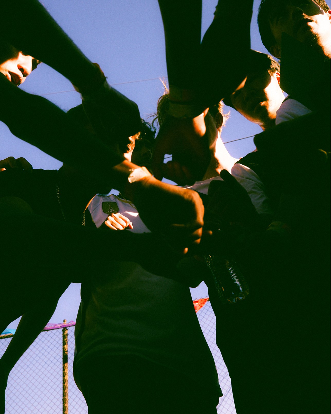 A group of people stand in a circle with their hands joined in the center, viewed from below against a clear sky.