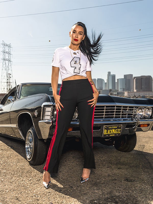 Woman in number 4 Raiders football jersey in front of classic American car