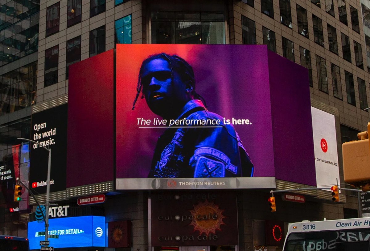 A digital billboard in Times Square displays a musician in blue and red lighting with the text, "The live performance is here.