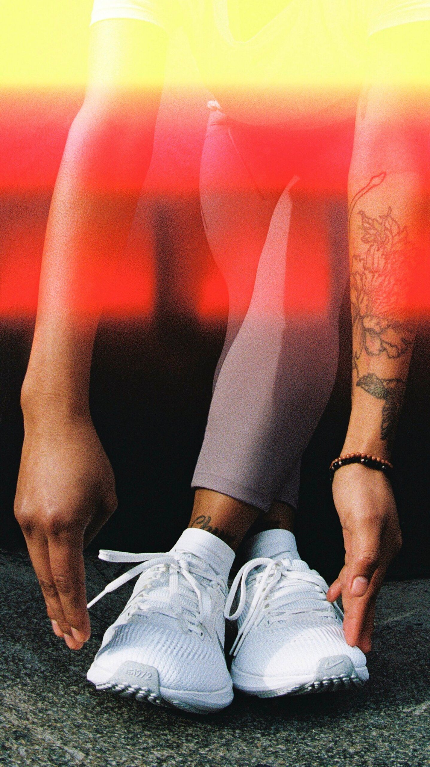 woman in cross legged forward fold. only lower half of body in shot. yellow and red light leak streaks at top of photo. Wearing white Nike Pegasus 40 running shoes