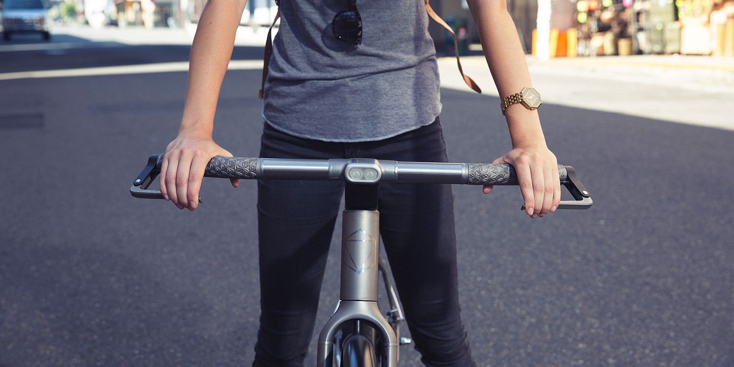 A person standing on a city street holding the handlebars of a 3D-printed scooter, only the torso and arms are visible.