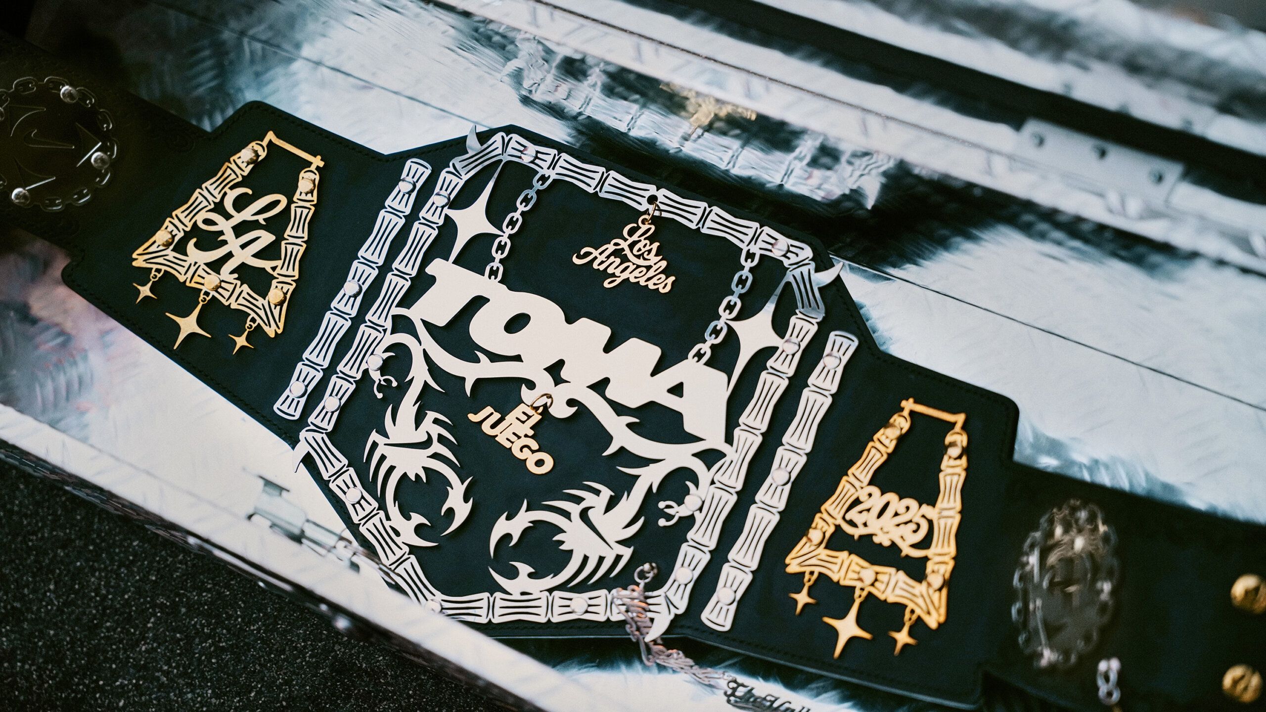A close-up of a black championship belt with gold and silver designs, featuring "Los Angeles," "TONA," "2023," and musical notes engraved on the front.