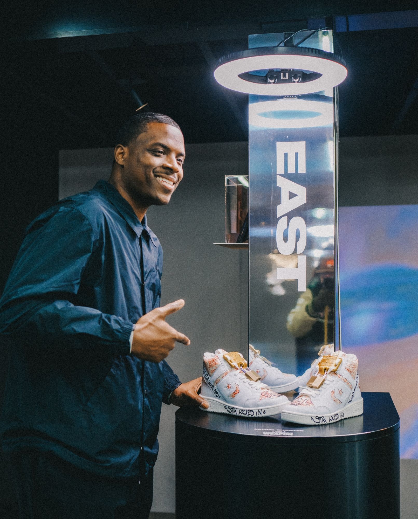 Artst, Lethal Shooter, smiles and points to a pair of Converse sneakers he designed