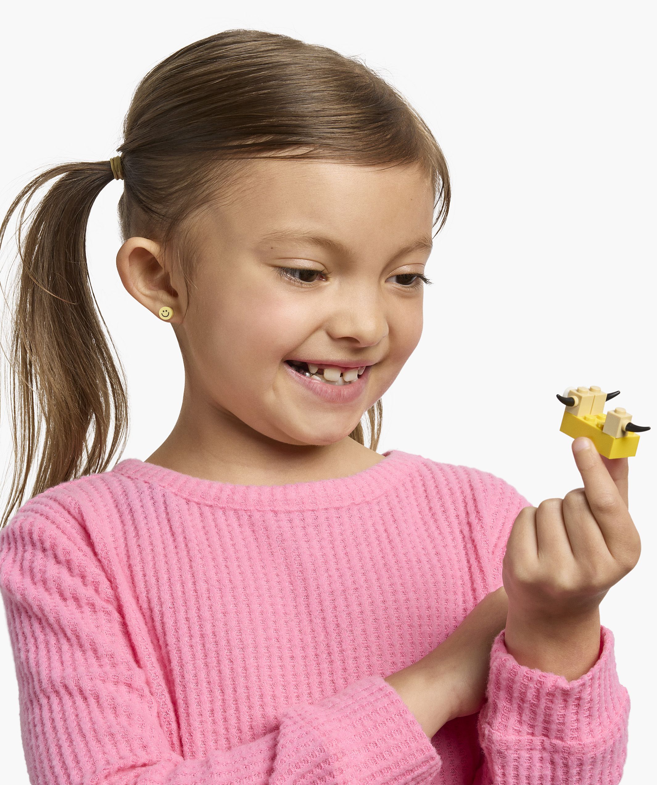 A child in a pink shirt looks at a small LEGO animal toy