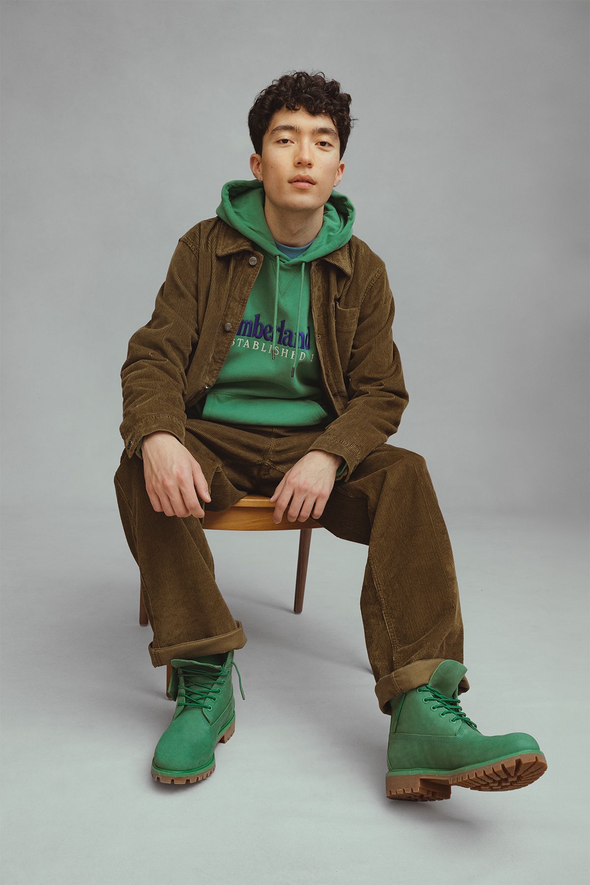 A man sitting on a chair in a green jacket and green boots.