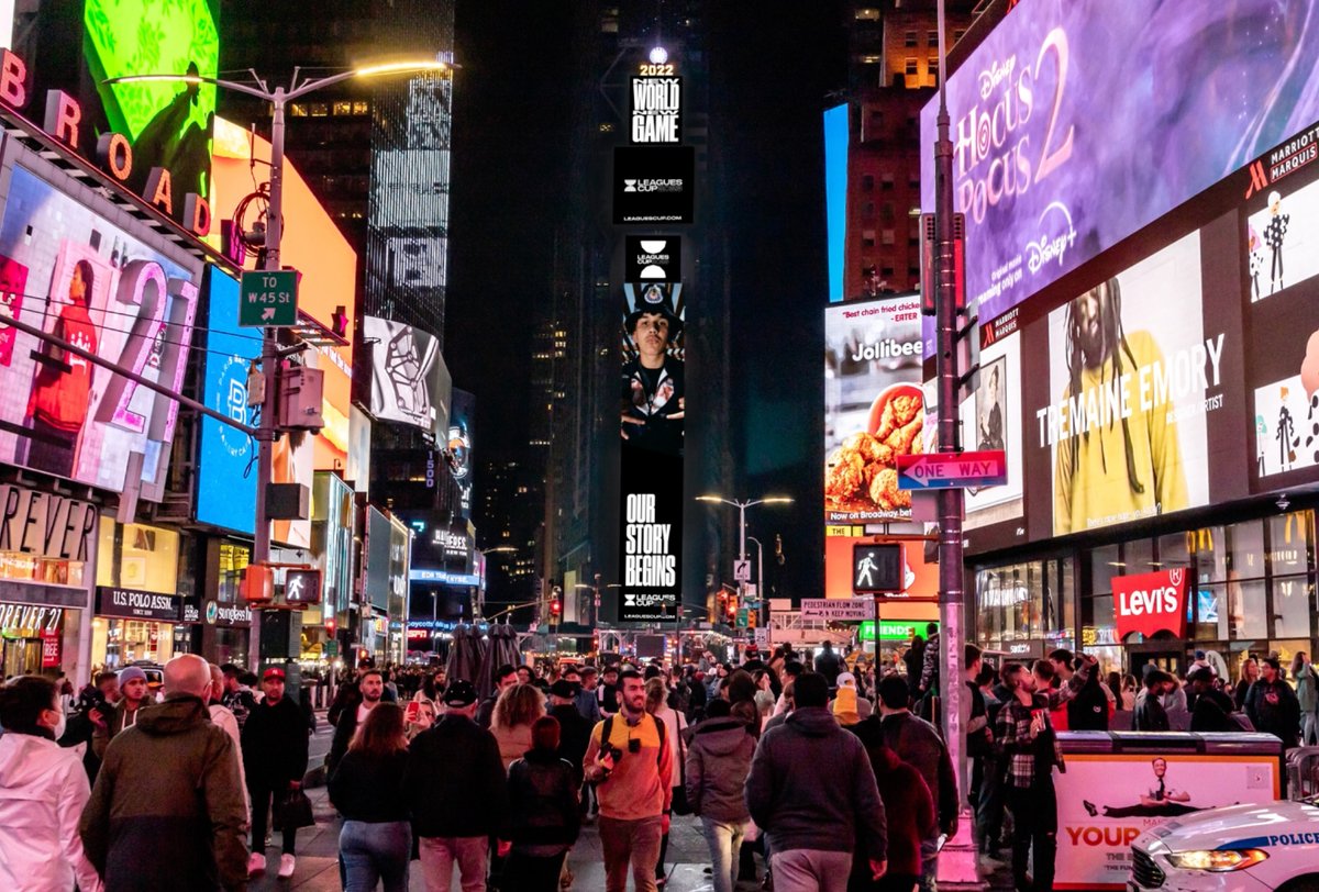 Crowds walk through Times Square at night, surrounded by bright digital billboards displaying advertisements and colorful lights.