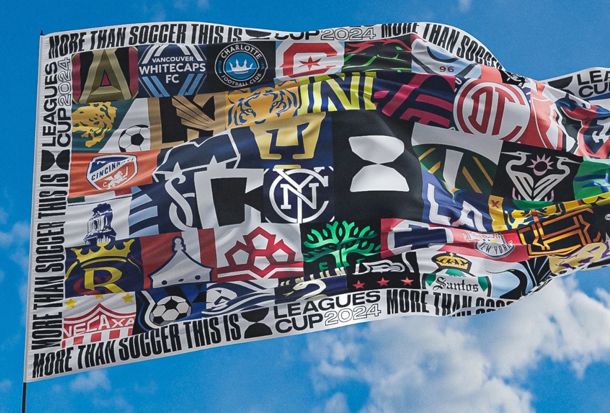 A flag featuring logos of various soccer teams from the Leagues Cup 2024 waves against a blue sky with clouds.