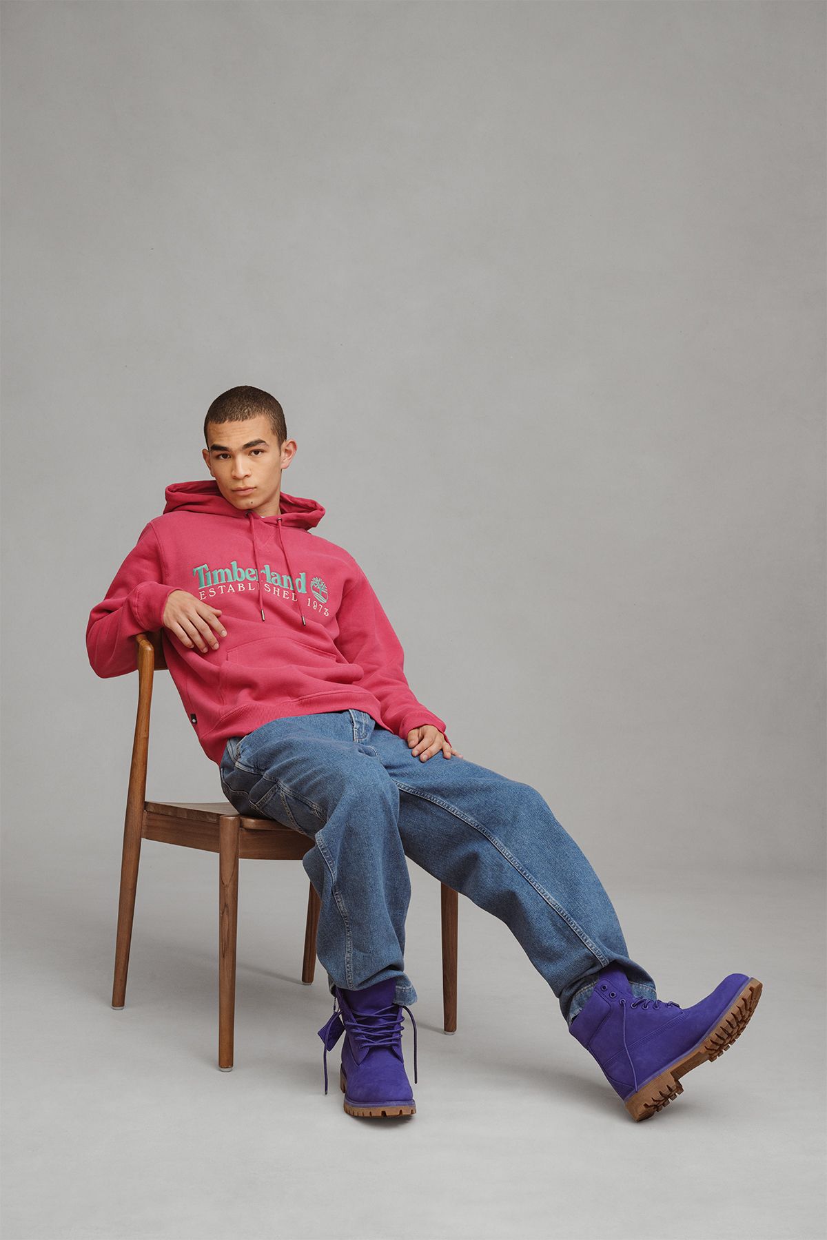 Man sitting ina chair with pink Timberland sweatshirt, blue jeans and clemantis blue timberland boots