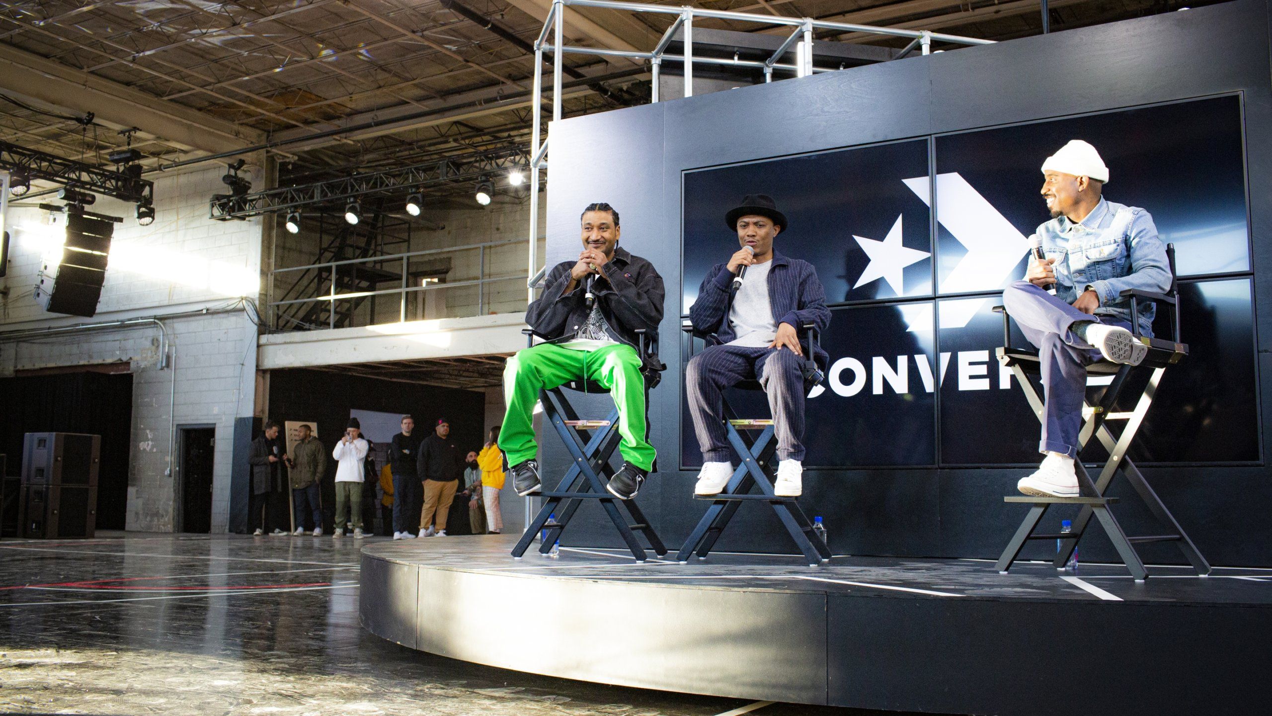 Panel of three artists sit in director's chairs with microphones in front of Converse back drop