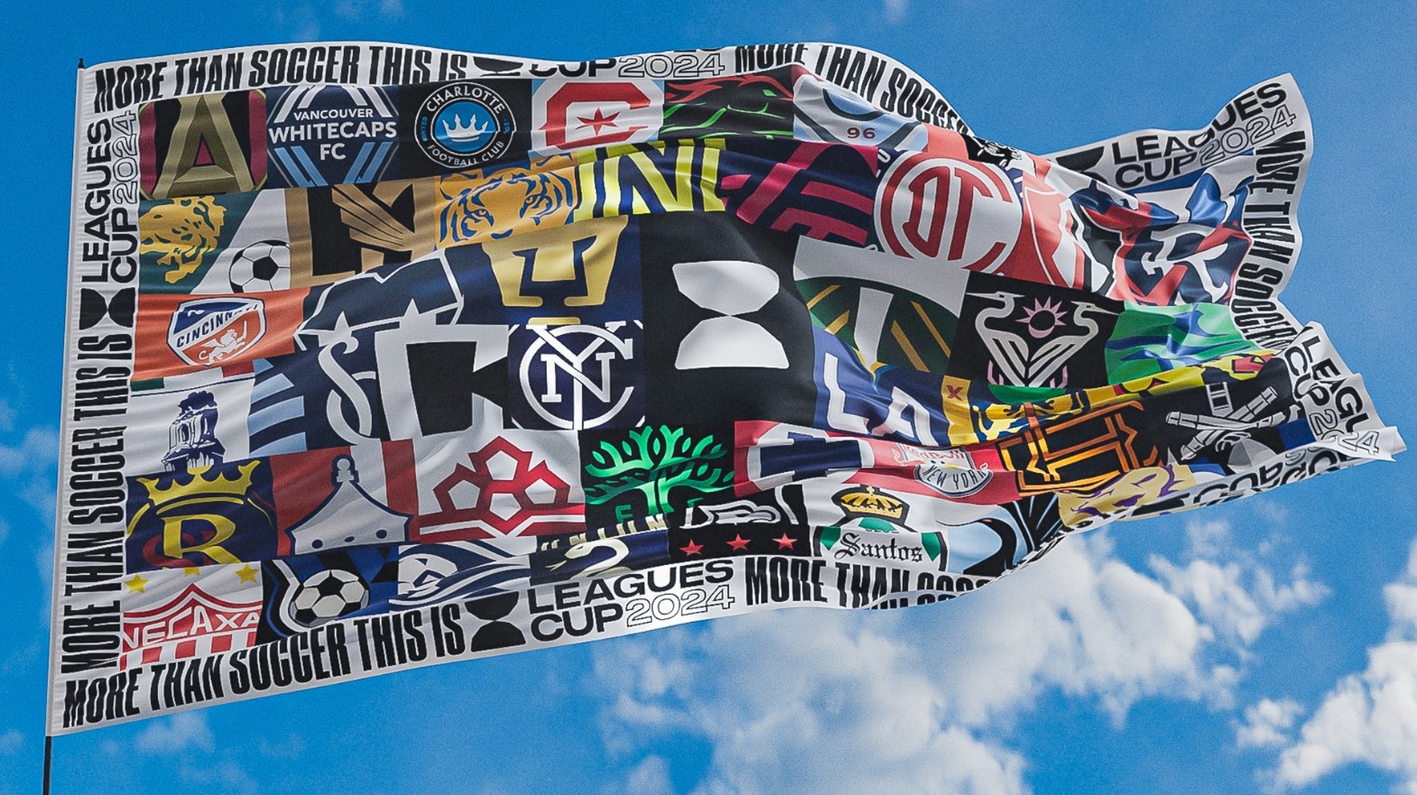 A large flag waves against a blue sky, displaying an array of soccer team logos and the text "More Than Soccer This Is" and "Leagues Cup 2024".