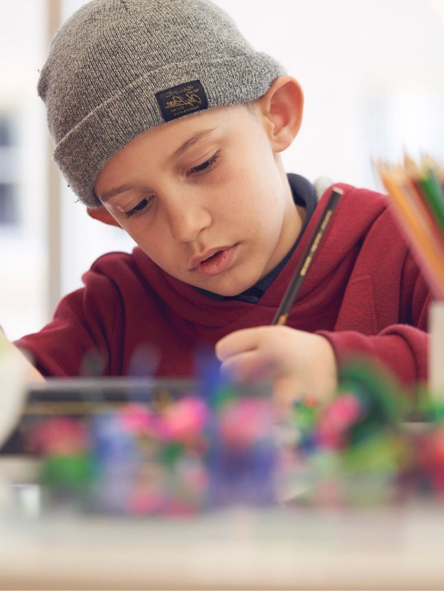 A young boy looks down concentrating while drawing with colored pencil