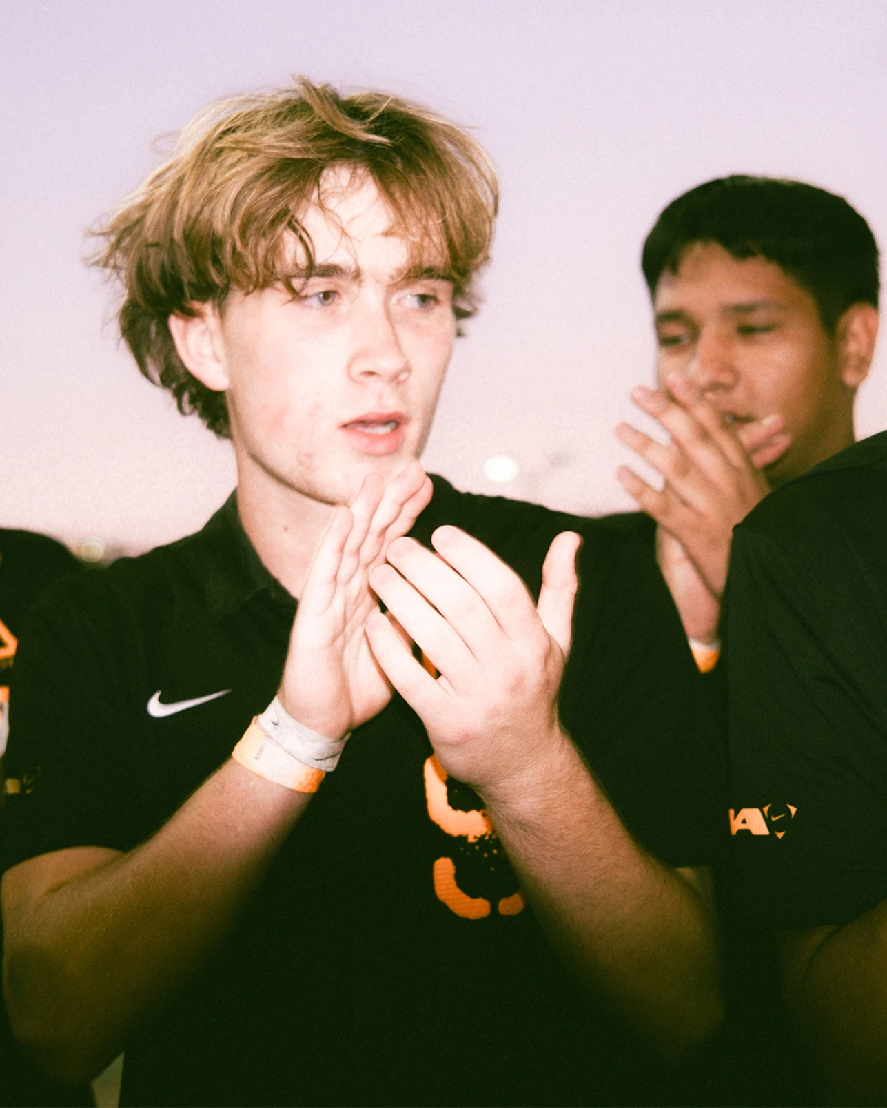 Two young men in black sports uniforms clap, with one in the foreground and the other slightly behind him.
