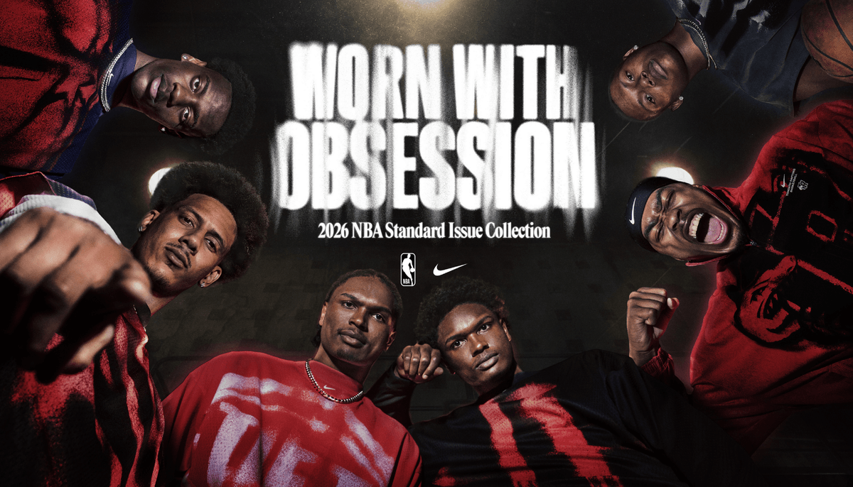 Six basketball players in red and black look down at the camera under bright lights; “Worn With Obsession, 2026 NBA Standard Issue Collection” text is displayed above them with NBA and Nike logos.