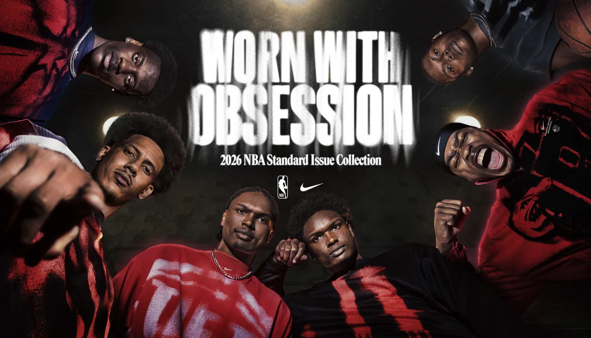Six basketball players in red and black look down at the camera under bright lights; “Worn With Obsession, 2026 NBA Standard Issue Collection” text is displayed above them with NBA and Nike logos.