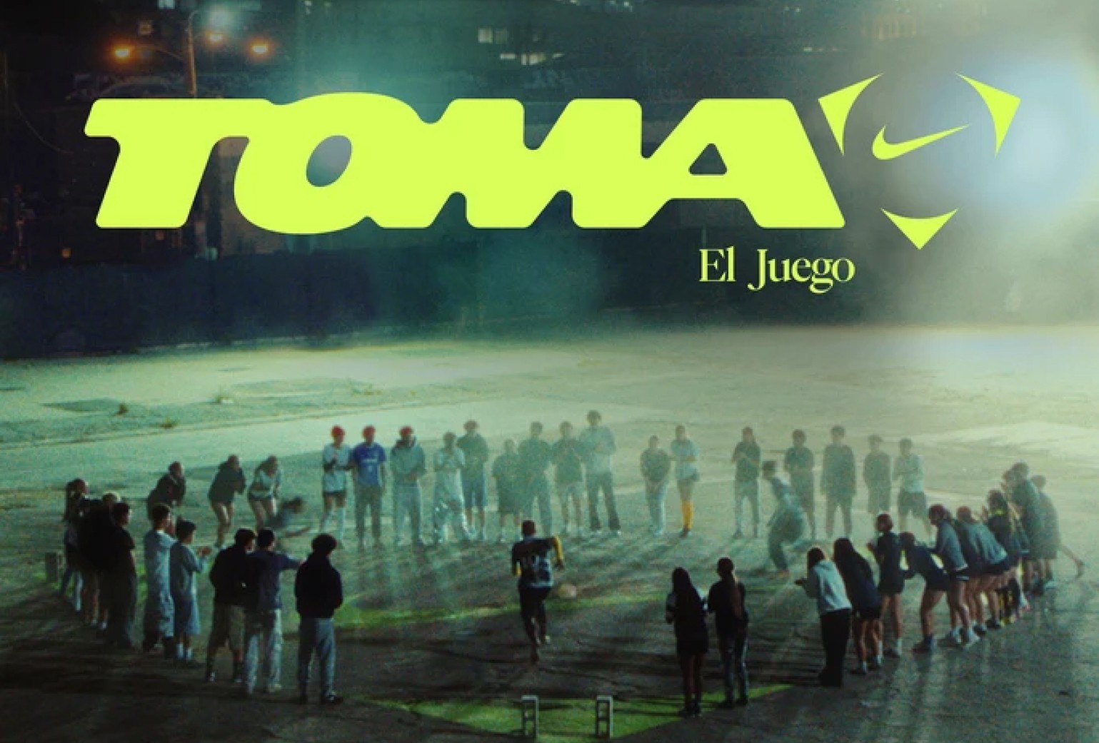 A group of people stands in a large circle on a concrete surface at night under the neon text "TOMA El Juego" with a prominent Nike logo above.