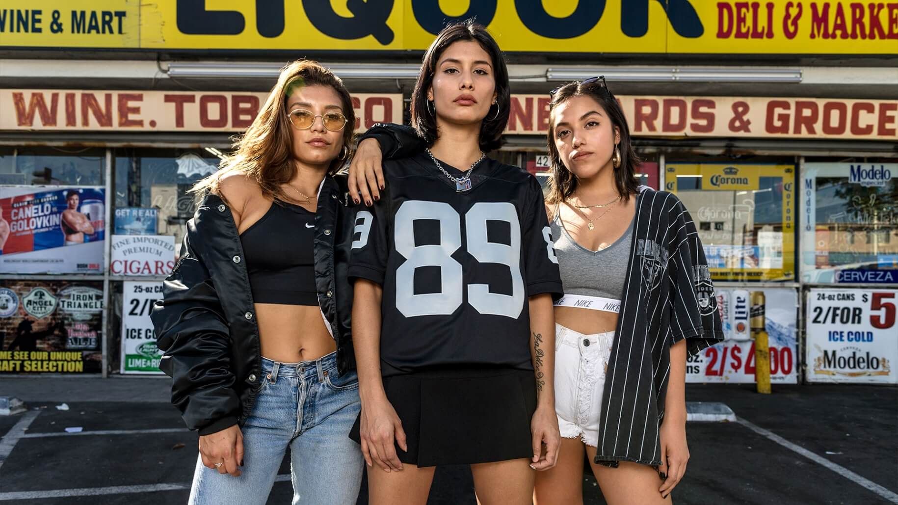 Three Women in front of liquor sttore wearing Raiders clothing and number 89 jersey