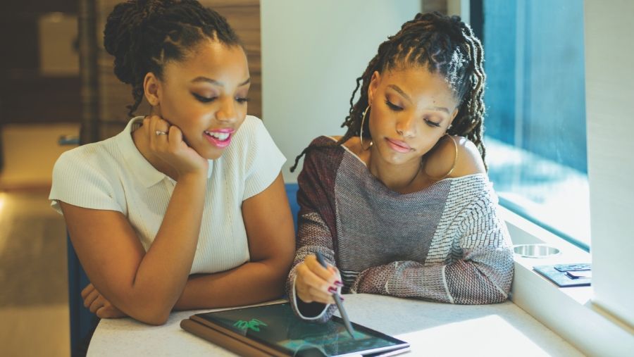 Chloe and Halle seated at table drawing with stylus on HP notebook