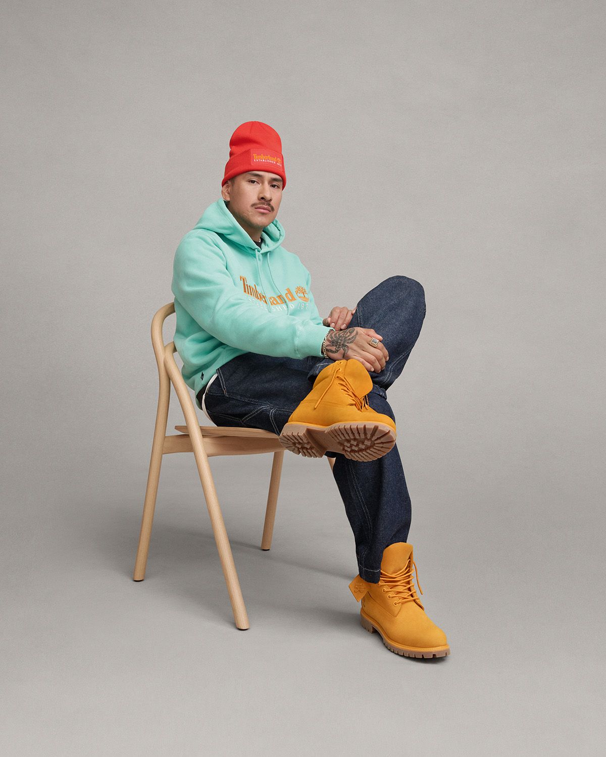 Man sitting in chair with orange timberland hat, light blue timberland sweatshirt, and dark cheddar timberland boots
