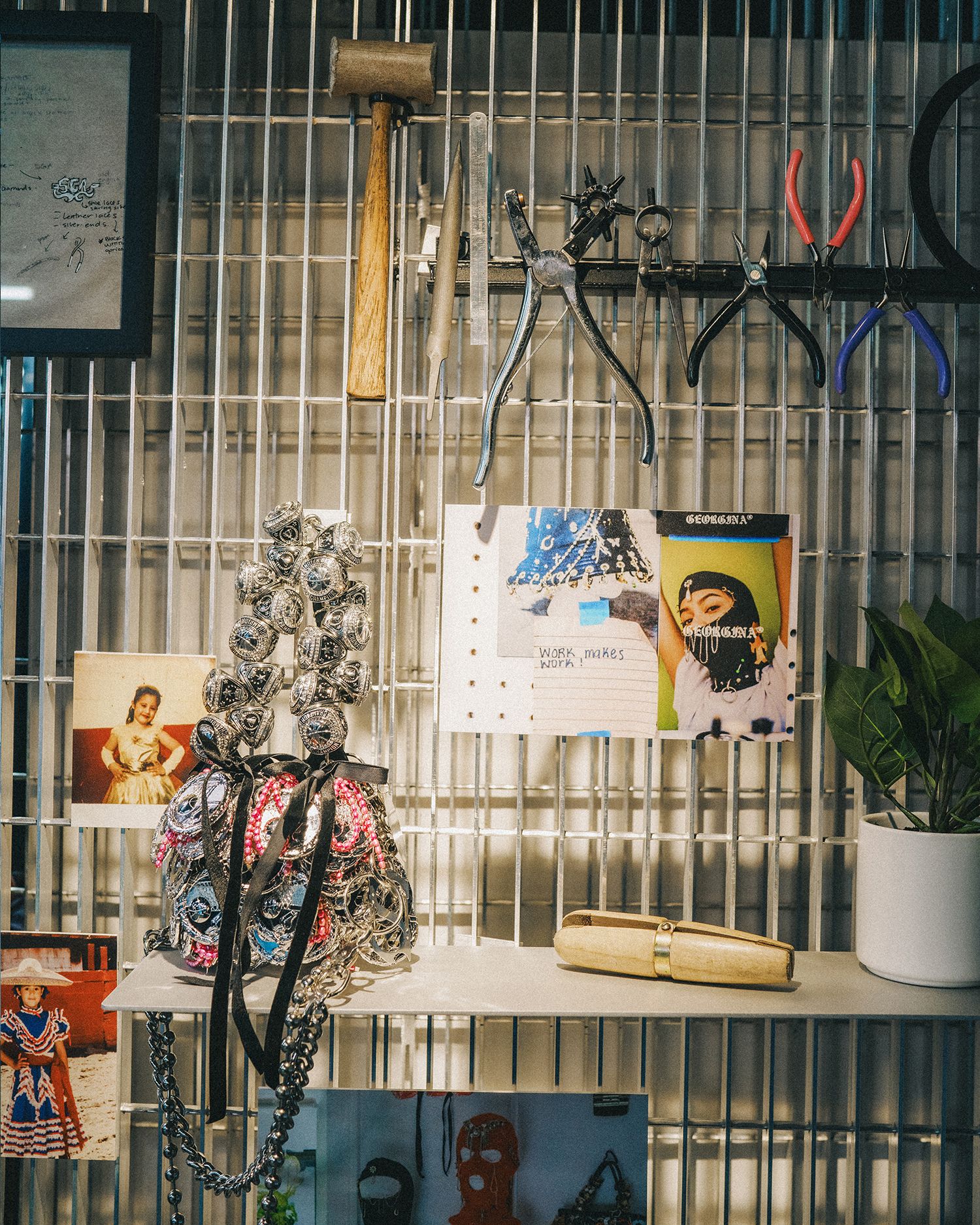 close up of Georgina's wall with jewelery making tools, photos and a note saying Work makes Work