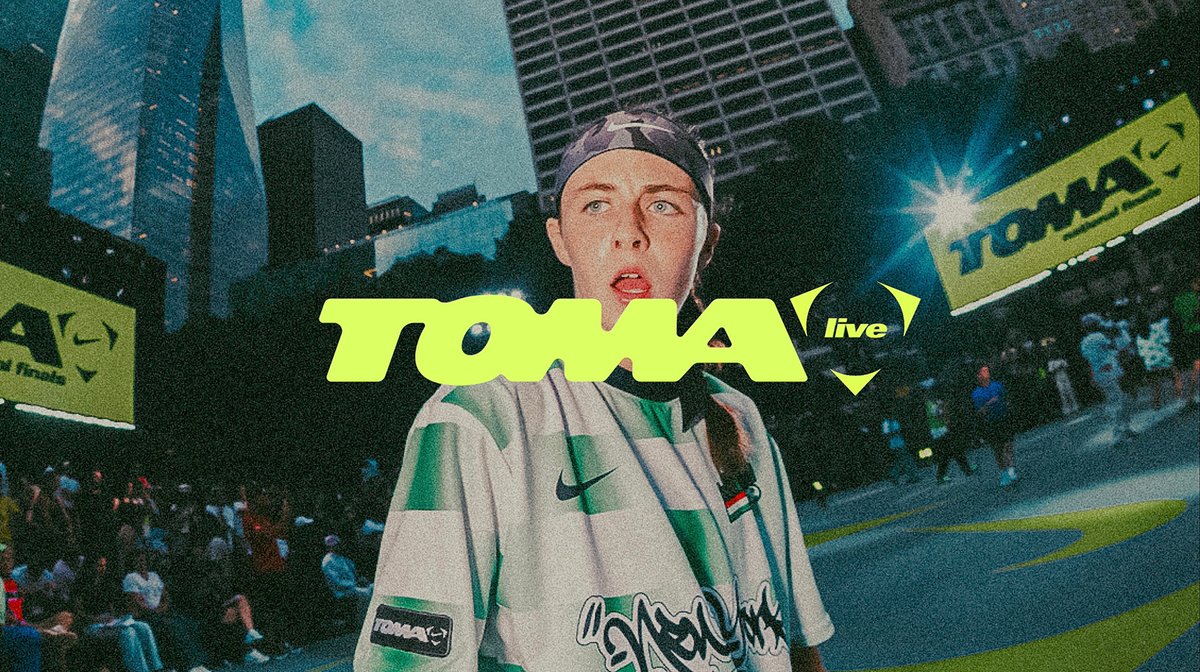 Person wearing a white and green jersey stands in front of a crowd at an outdoor event, with large “TOMA live” signs displayed on screens in the background.