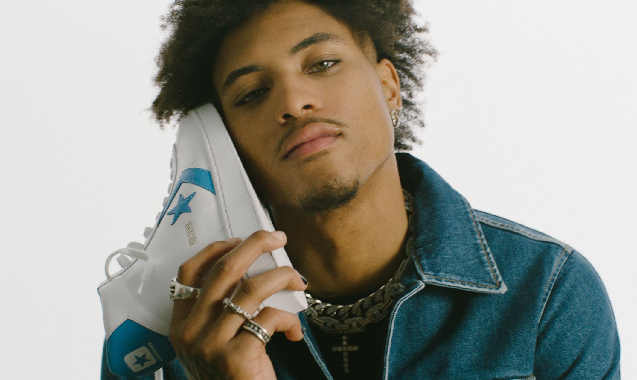 Kelly Oubre Jr holding white and blue converse pro leather high top shoe up to side of his face