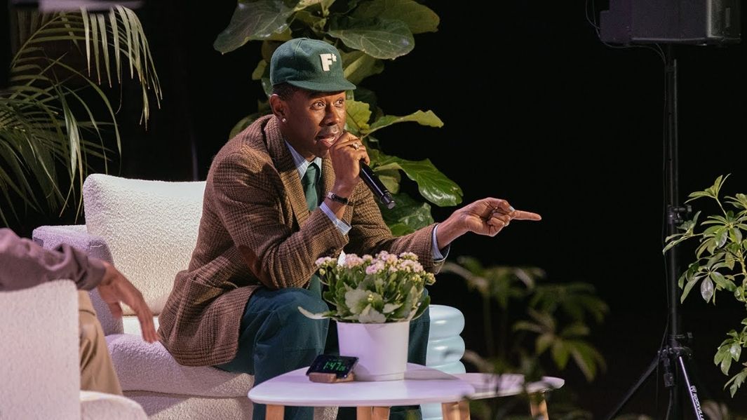 John Boyega with microphone sitting giving a talk with plants behind him
