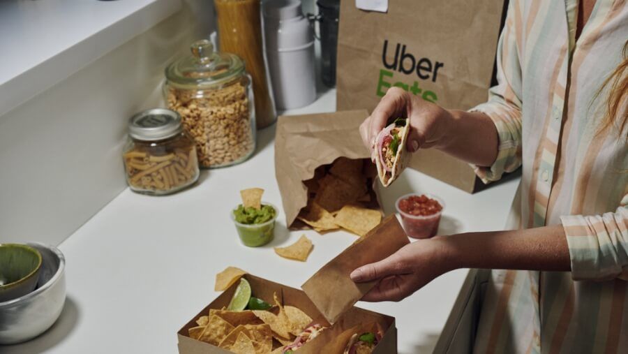 Woman holding taco from Uber Eats bag on kitchen counter
