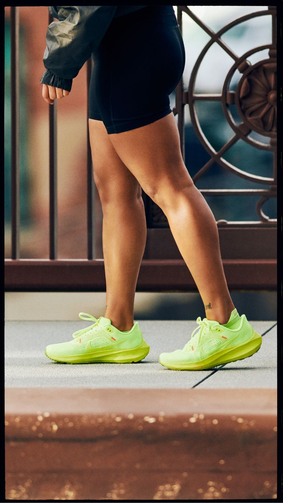 Woman walking on sidewalk wearing black shorts and bright green Nike Pegasus 40 running shoes