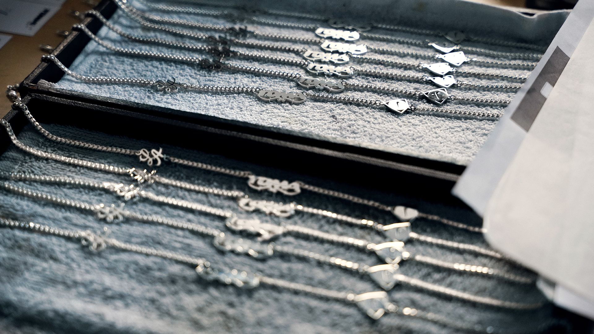 Several silver necklaces with various pendants are laid out in rows on a soft fabric surface for display or inspection.