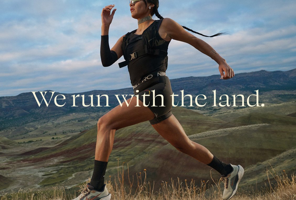 A person in athletic gear runs outdoors over grassy hills with mountains in the background. Text reads, "We run with the land.