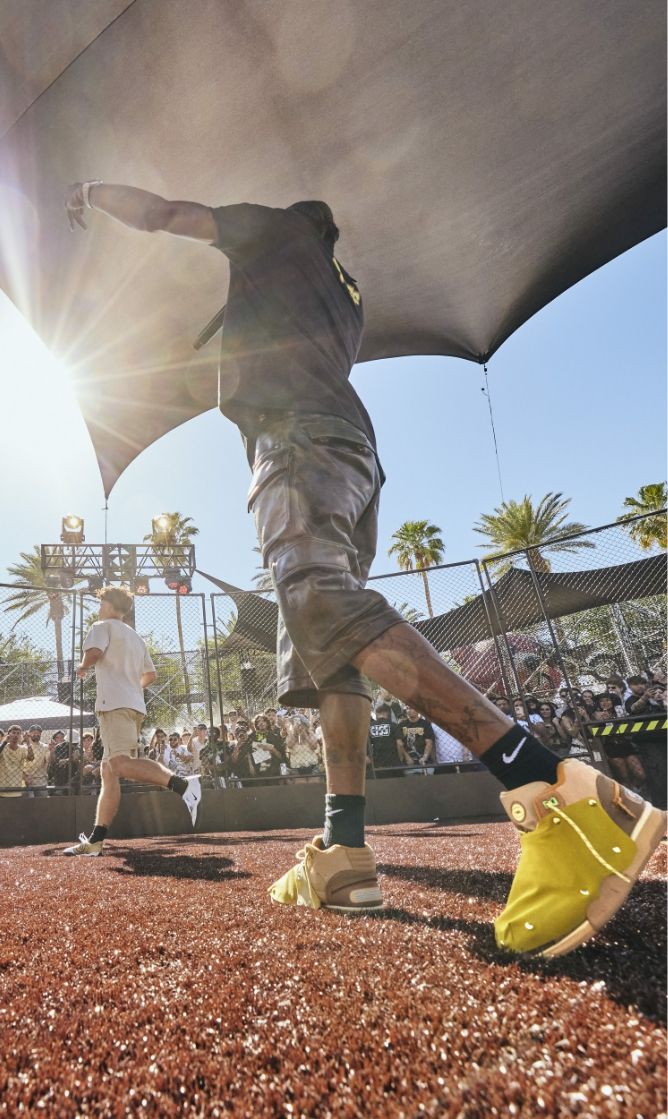 A basketball player wearing yellow sneakers prepares to throw a ball on an outdoor court during a daytime event, with a crowd and palm trees in the background.